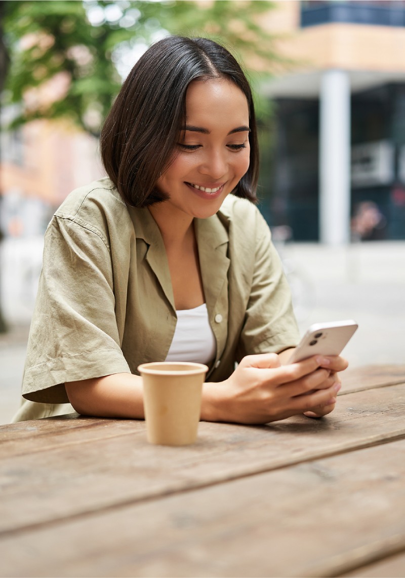 A woman using her phone to book an appointment while seated at an outdoor table